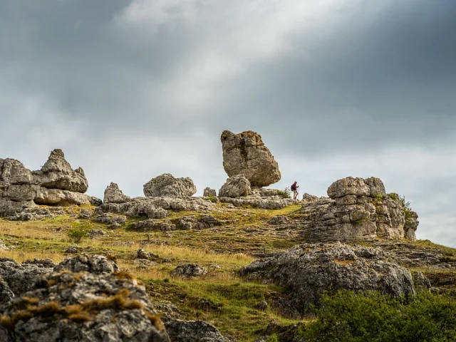 Un randonneur se balade à travers un ensemble de grandes roches aux formes variées formant le chaos de Nîmes-le-Vieux sur le Causse Méjean