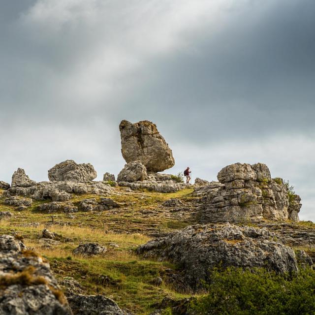 Un randonneur se balade à travers un ensemble de grandes roches aux formes variées formant le chaos de Nîmes-le-Vieux sur le Causse Méjean